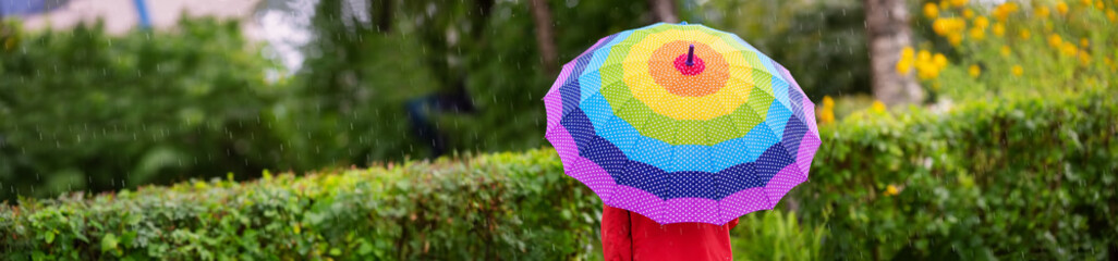 Boy holding colourful umbrella under rain in summer