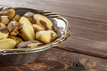 Lot of whole unshelled brazil nut in old iron bowl on brown wood
