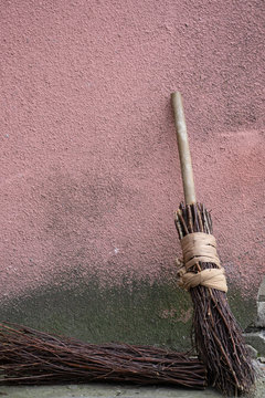 An old broom stands near the old pink wall. The wall below turned black. Another broom lies below. Vertical orientation