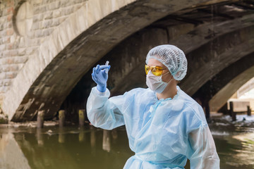female ecologist looks at a test tube with water from a city river