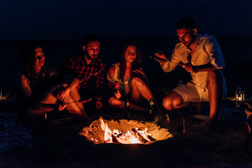 Group of friends partying on the beach sitting around the fire