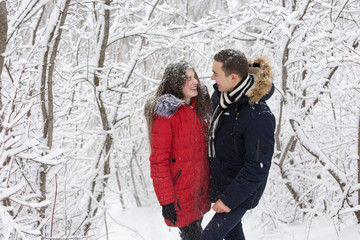 Fototapeta na wymiar The guy and the girl have a rest in the winter woods. Husband and wife in the snow. Young couple walking in winter park 
