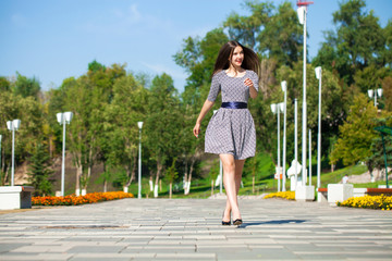 Young beautiful woman in gray dress walking on the summer street