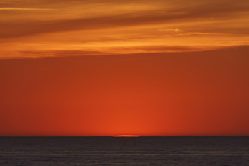    Red-violet sunset over the Atlantic ocean. White disc of the sun over the red sea at sunset. Natural bright background is suitable for postcard, touristic guide, greeting card.