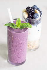 Smoothies of banana, blueberry, blackberry, oatmeal and yogurt and ingredients in two glasses on a light background