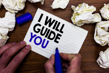 Writing note showing I Will Guide You. Business photo showcasing Help showing a route Influence to do or think something Hand holding marker write words paper lob scatter around woody desk