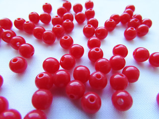 Bright red round beads for needlework are randomly scattered over a white background.