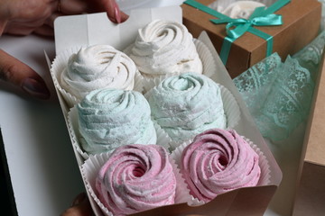 Woman puts marshmallows of different colors into gift boxes. Nearby colored ribbons for bandaging boxes.
