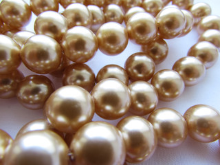 Beautiful mother-of-pearl light beige pastel big beads on a thread lie on a white fabric background.