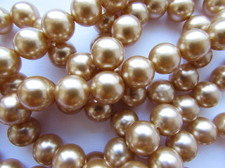 Beautiful mother-of-pearl light beige pastel big beads on a thread lie on a white fabric background.