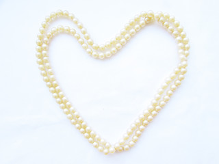 Gentle light natural small pearl long beads in the shape of a big heart on a white background.