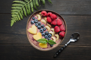 Healthy tropical breakfast banana and blueberry smoothie decorated with fruits in coconut bowl on wooden board. View from above. Clean eating, vegetarian food concept.