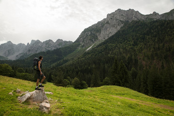 Caucasian man with a trekking backpack standing on a rock and admiring the beautiful mountain landscape. Connection between human being and nature concept