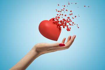 Close-up of woman's hand facing up and levitating red valentine heart that has started to...