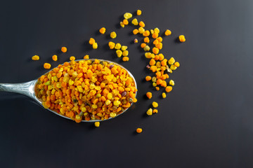 Honey bee pollen granules in the spoon on the dark background