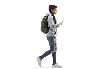 Fototapeta Female student with a backpack walking and looking into a mobile phone obraz