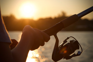 A boy fishing at sunset, close up on rod and reel