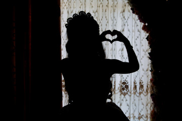 The bride looks out of the huge window in the bridal suite revealing the backside of the wedding dress . The back side of a white wedding dholds a heart in his handress.