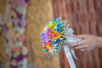 He holds a wedding flower in his hand . coloured macro photo of a detailed bouquet with colorfull roses, white small flowers and a fake diamond in the centre of the rose .