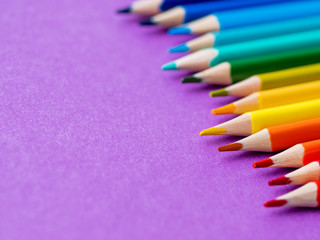 Row of colorful watercolor pencils on lilac background. School supplies on purple paper background. Kid's stationery. Back to school magenta backdrop.