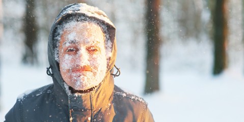 Fun portrait of an young frozen man. Jogging in a blizzard in the woods. Face covered with snow and...