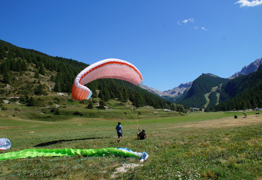 Paragliders training and landing on an alpine pasture with the summits in background