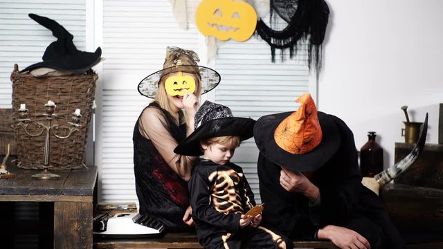Happy family mother father and son in costumes on celebration of Halloween. Halloween celebration concept. Dad with mom and their son in hats and skeleton suit. Wizard, witch and little skeleton.