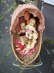 Skurril anmutende Puppen in einem alten Kinderwagen aus Korbgeflecht auf dem Flohmarkt und...