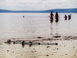 Fototapeta na wymiar Crutches on a sand by water. People silhouettes in water, Selective focus. Concept healthcare, Water recovery procedure.