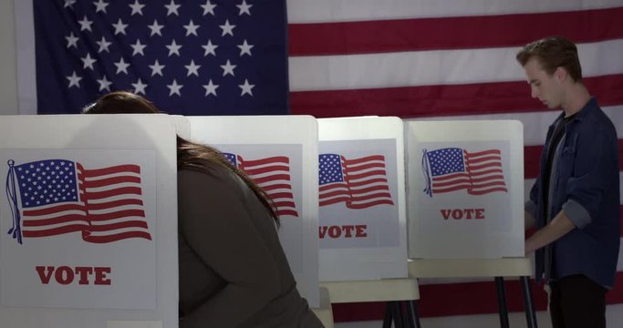 MS Series of voters of various demographics arriving and leaving to vote in booths at polling station with US flag. Locked off sequence with dissolves, real time 4K