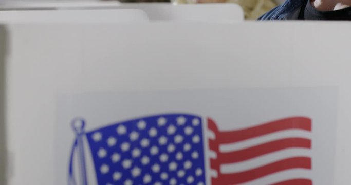 BCU crane move up from booths to young man casting vote with others at polling station. He looks up to think and looks down again. Slow motion 4K 60fps