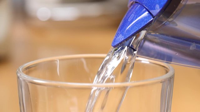 Pouring clean water from filter container into glass. Water filtration process at home