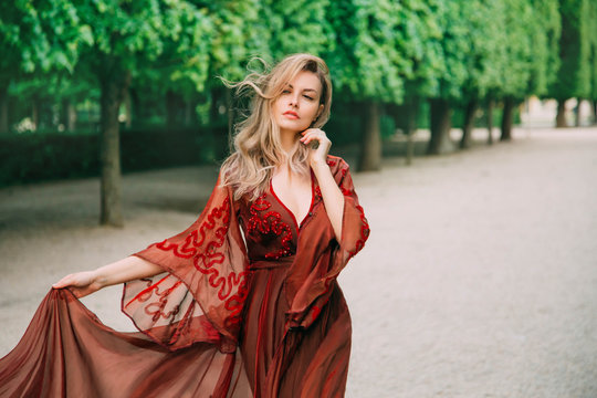 Portrait of a blond woman with flying hair in a red, wine color dress. Gentle makeup, Natural beauty with minimal retouching and without processing. Bloody Countess Bathory. Art horizontal photography