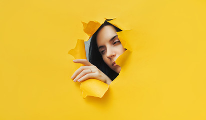 A girl with a cunning expression. Portrait of a woman looking through the hole in yellow paper. Distrustful look. Women's curiosity and gossip. A jealous wife.
