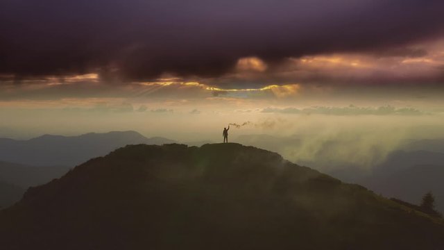 The male with a smoke bomb standing on a mountain against the sunrise