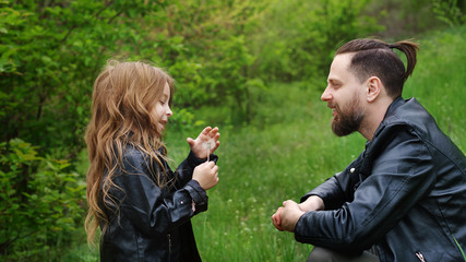 Obraz premium Modern stylish family walking in park. Daughter enjoys chatting with dad. Lovely moments spent to father in nature. Time together. Family look. Urban casual outfit. Trigger memories of childhood
