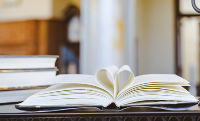 Close-up, The book on the ground is open pages are forming hart a symbol of love.Book in library with old open textbook, stack piles of literature text archive on reading desk, 