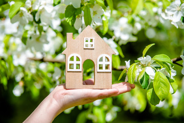 The girl holds the house symbol against the background of blossoming appletree 