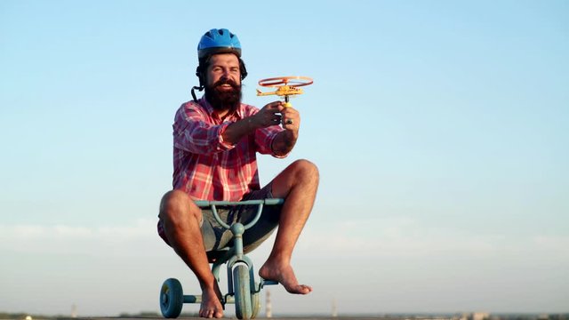 Bearded funny man have fun riding on kids bicycle on sky background. A funny bearded man is riding a kids bicycle . Funny man having fun on children bicycle.