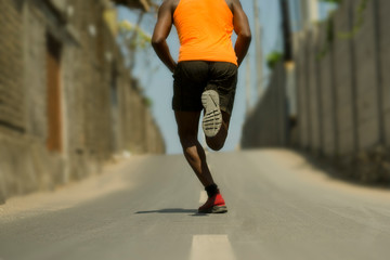 Fototapeta premium Back view of athletic black African American professional sport man running training hard outdoors on asphalt road during jogging workout in healthy lifestyle