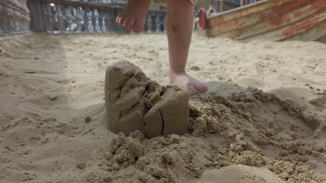 Shot of a child's legs stomping on a small sand castle.
