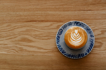 Drinking cup of coffee during day helps to refresh and relax. A  beautiful leaf-shaped latte art on wooden floors and space in the coffee shop. Caffeine makes people alert and increases energy levels.