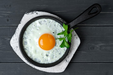 fried eggs in cast iron pan on white wooden stand with parsley