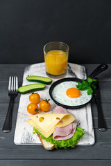 Breakfast of toasts with cheese, ham, lettuce, scrambled eggs in pan, cherry tomatoes, cucumbers and orange juice. Serve on cutting board. Nutritious breakfast.