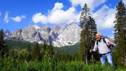 Naklejka na ściany i meble aktiver Senior wandert im tiefen Gras in den Bergen in Südtirol vor herrlichem Panorama