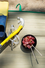 Overhead view of swim mask, snorkel, fins, and ahi tuna fish poke with chopsticks on woven straw...