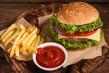 Tasty grilled homemade burgers with beef, tomato, cheese, cucumber and lettuce. Delicious grilled burgers. Craft beef burger and french fries on wooden table