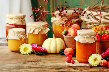Jams in glass jars among fruits and vegetables.