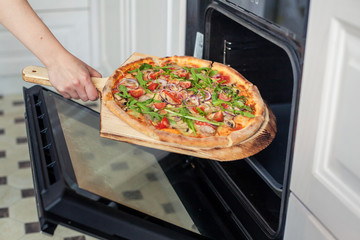 Close-up. Woman hand put pizza in the oven.
