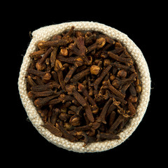 Dry cloves in a bag isolated on black background. View from above. Seasoning on isolate. Dry spices.